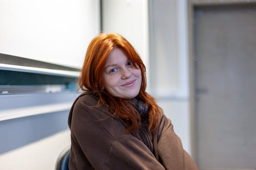Portrait of a smiling young woman with red hair seated in a classroom.