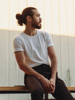 A young man in casual attire sitting thoughtfully on a bench outdoors.