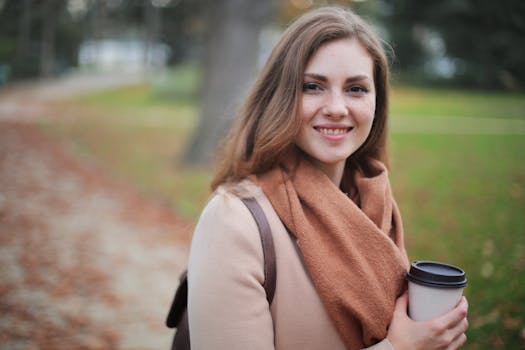 Portrait of a smiling woman holding a coffee cup in a serene autumn park setting.
